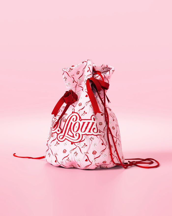 Vaaleanpunainen kiristysnyörillinen laukku, jossa punaiset rusetit ja juhlava design "P.Louis" -brändillä vaaleanpunaisella taustalla