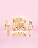 P.Louise Teddy Glitter Bad Bitch Energy Lip Duo kookoskakun tuoksussa, jossa huulihoitoaine ja huuliöljy vaaleanpunaista taustaa vasten