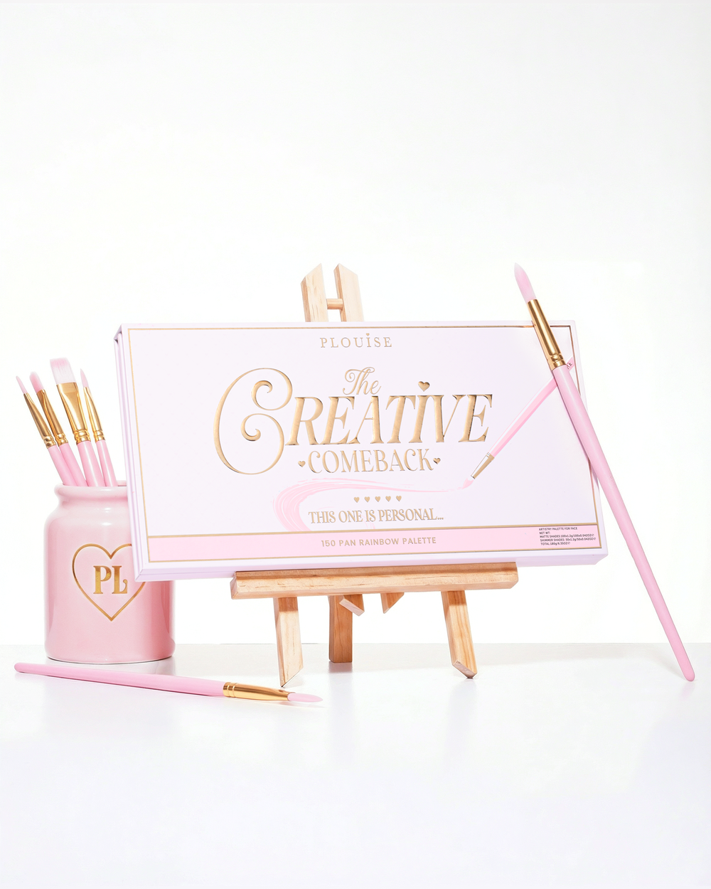 Suljettu vaaleanpunainen P.Louise Creative Comeback XXXL Rainbow Eyeshadow Palette asetettu taidetelineeseen, jota ympäröivät meikkisiveltimet