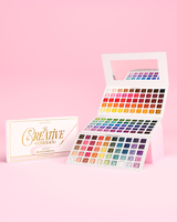 Avaa P.Louise Creative Comeback XXXL Rainbow Eyeshadow paletti vaaleanpunaista taustaa vasten ja sen vieressä oleva vaaleanpunainen pakkauslaatikko