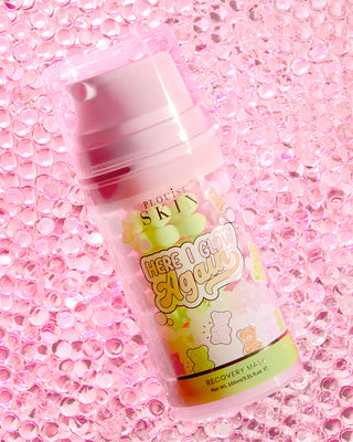 A bottle of P.Louise Here I Glow Again Recovery Mask in candy bears scent with a pink and green label, featuring illustrations of candy bears, placed on a pink glittery background.