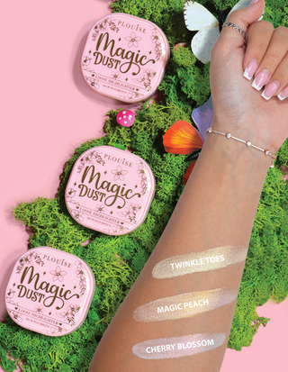 Kolme kompaktia löysää korostustuotetta Magic Dust -sävyissä Twinkle Toes, Magic Peach ja Cherry Blossom, kädessä kukka taustalla.
