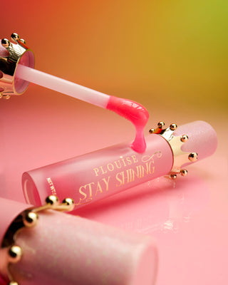Lähikuva P.Louise Stay Shining Crown Lip Oil -pullosta, jonka korkin ympärillä on kullanvärinen kruunu ja vaaleanpunainen applikaattorisauva, jossa näkyy tuotteen rakenne ja hienovarainen vaaleanpunainen väri.