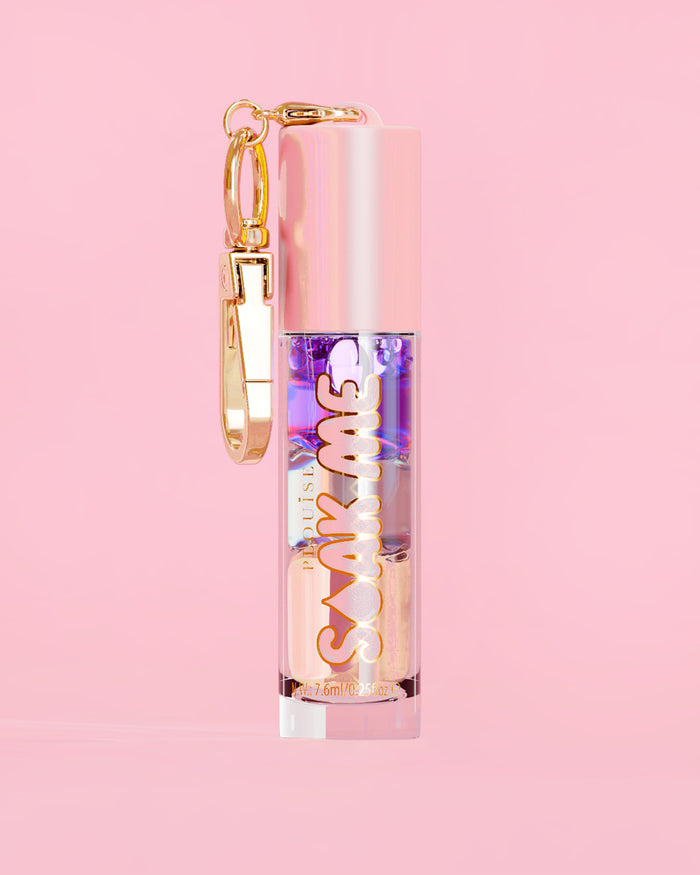 P. Louise Soak Me Lip Oil värikkäällä kerroksisella öljyllä vaaleanpunaisessa putkessa, jossa on kultainen hakas vaaleanpunaisella taustalla