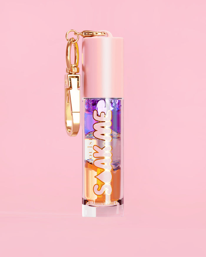 P. Louise Soak Me Lip Oil värikkäällä kerroksisella öljyllä vaaleanpunaisessa putkessa, jossa on kultainen hakas vaaleanpunaisella taustalla