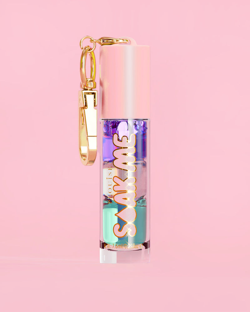 P. Louise Soak Me Lip Oil värikkäällä kerroksisella öljyllä vaaleanpunaisessa putkessa, jossa on kultainen hakas vaaleanpunaisella taustalla