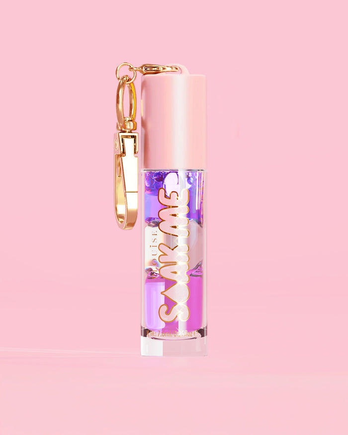 P. Louise Soak Me Lip Oil värikkäällä kerroksisella öljyllä vaaleanpunaisessa putkessa, jossa on kultainen hakas vaaleanpunaisella taustalla