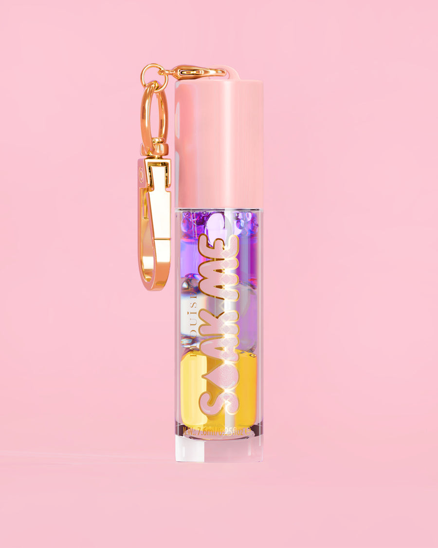 P. Louise Soak Me Lip Oil värikkäällä kerroksisella öljyllä vaaleanpunaisessa putkessa, jossa on kultainen hakas vaaleanpunaisella taustalla