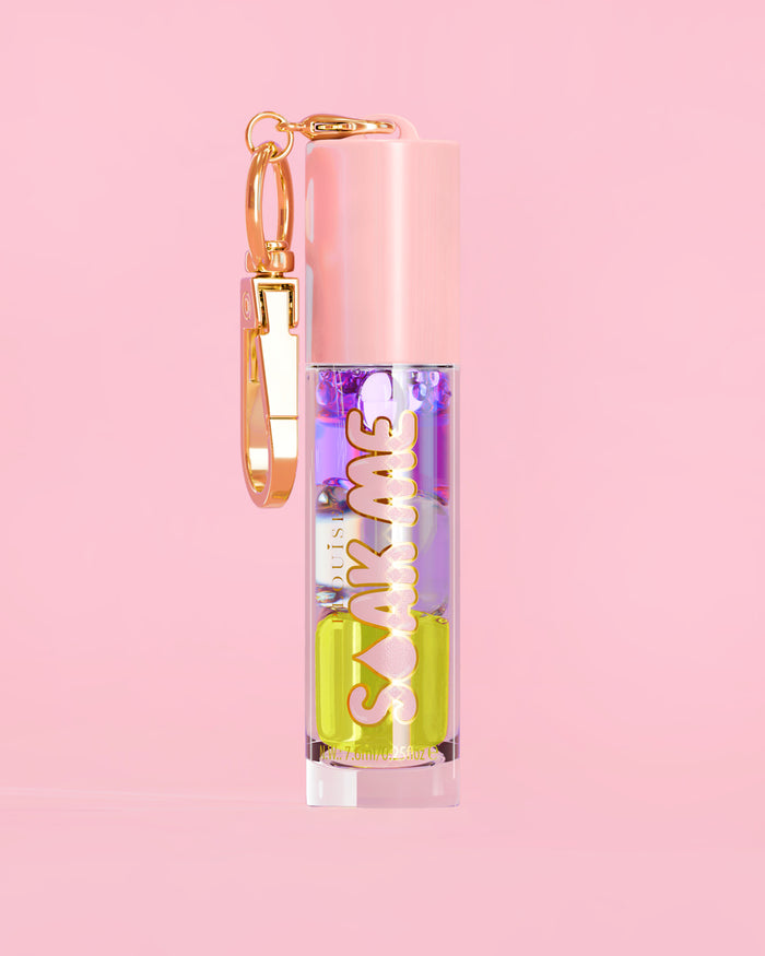 P. Louise Soak Me Lip Oil värikkäällä kerroksisella öljyllä vaaleanpunaisessa putkessa, jossa on kultainen hakas vaaleanpunaisella taustalla
