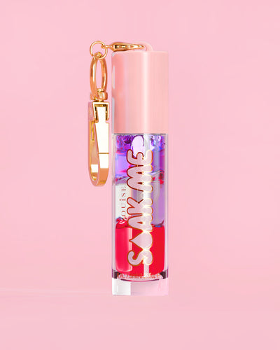 P. Louise Soak Me Lip Oil värikkäällä kerroksisella öljyllä vaaleanpunaisessa putkessa, jossa on kultainen hakas vaaleanpunaisella taustalla
