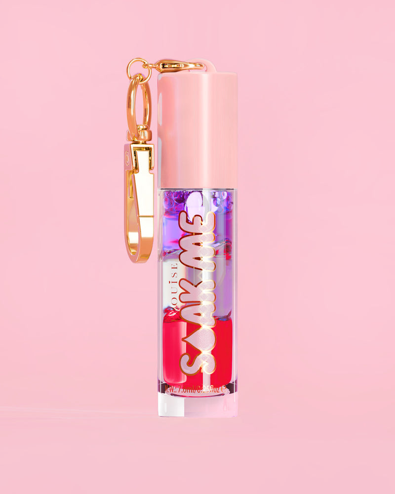 P. Louise Soak Me Lip Oil värikkäällä kerroksisella öljyllä vaaleanpunaisessa putkessa, jossa on kultainen hakas vaaleanpunaisella taustalla